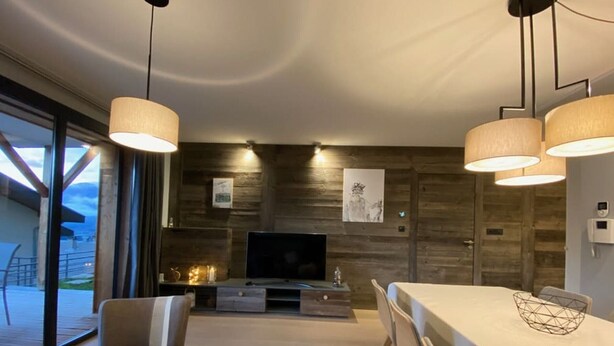 A modern living room with a large TV, wooden wall paneling, and a dining area with a table and chairs. - 4-Room Apartment, 6 People, Sauna, Hammam, Parking, Wifi (Châtel)
