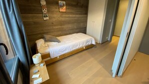 A small bedroom with a wooden headboard, a single bed, a bedside table with a cup and papers, and a door leading to another room. - 4-Room Apartment, 6 People, Sauna, Hammam, Parking, Wifi (Châtel)