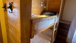 Una camera con letti a castello, pareti in legno, una piccola finestra e un punto luce a parete.