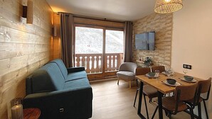 Una stanza accogliente con arredamento in legno, un divano, un tavolo da pranzo con sedie e un televisore montato a parete.