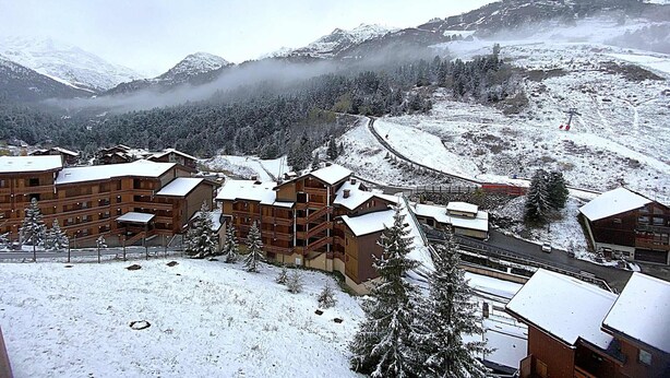 Una località montana innevata con edifici in legno, una seggiovia e una valle.