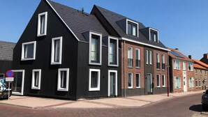 Un bâtiment moderne à deux étages, doté d’une façade noire et de cadres de fenêtres blancs, situé dans une rue dont le trottoir est pavé de briques.