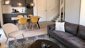 Un salon moderne avec un canapé gris, une table basse et un coin repas comprenant des chaises jaunes et une table en bois.