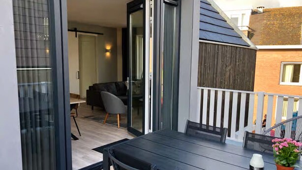 Un balcon extérieur avec une table et des chaises, un pot de fleurs et une vue sur un quartier résidentiel.