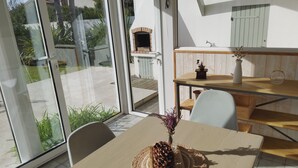 Een eethoek met een tafel gedekt voor twee personen, een rustieke houten tafel en uitzicht op het buitenterras door grote glazen deuren.