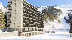 A multi-story hotel with balconies, located in a snowy mountainous area with ski slopes visible in the background. - 3-room Apartment for 8 People - Comfort (Araches-la-Frasse)