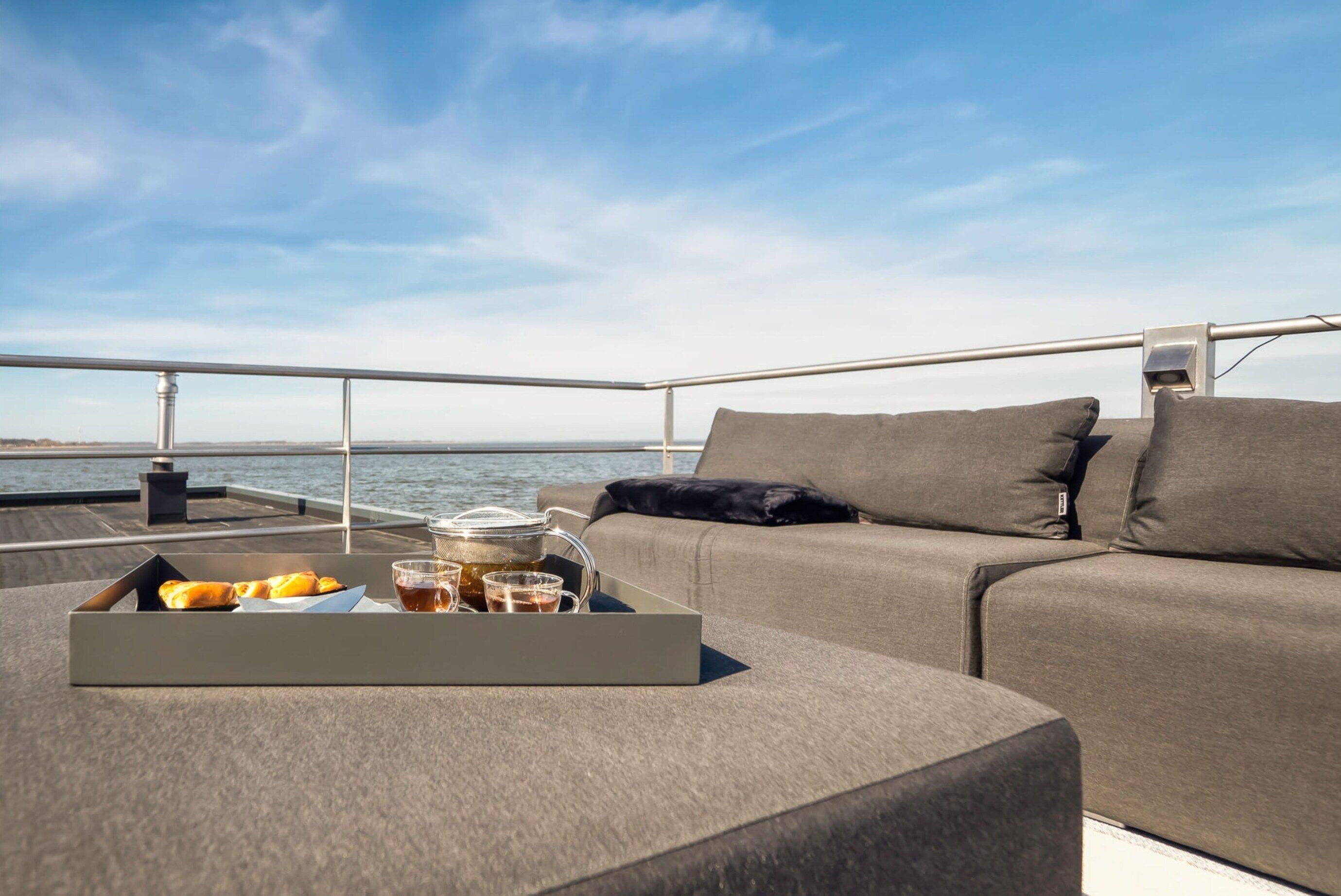 A deck with a sofa and a tray of pastries and drinks.