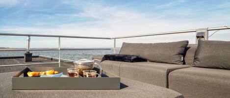 A deck with a sofa and a tray of pastries and drinks.