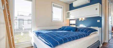 A bedroom with a bed, a window, a ladder, and built-in shelving.
