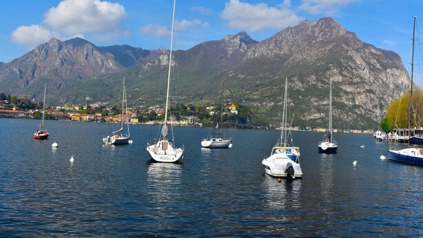 Ein Yachthafen mit mehreren Segelbooten, umgeben von Bergen und einer Stadt im Hintergrund.