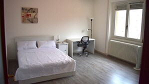Ein Schlafzimmer mit Bett, Schreibtisch, Stuhl, Heizkörper und Fenster.