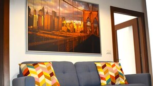 Ein modernes Wohnzimmer mit einem blauen Sofa, farbenfrohen geometrischen Kissen und einem großen Stadtbild an der Wand.