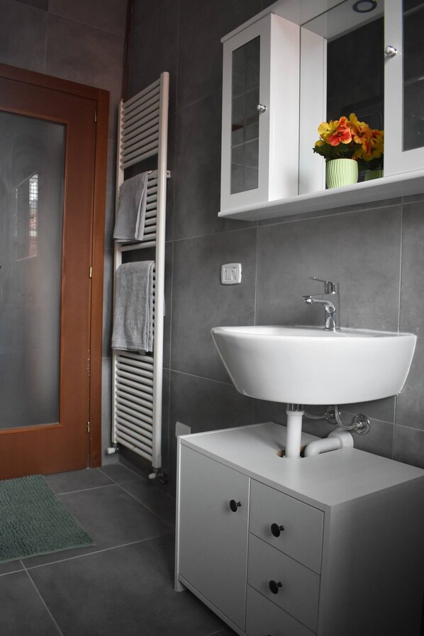 A bathroom with a white sink, a mirror cabinet, and a towel rack.