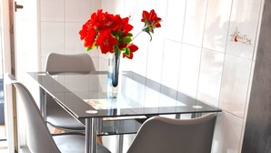 Ein moderner Essbereich mit einem Glastisch, grauen Stühlen und einer Vase mit roten Blumen.