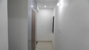 A narrow, well-lit hallway with white walls and a tiled floor, leading to a staircase. - Hotel Shree Radhe Laxmi (Khatoo)