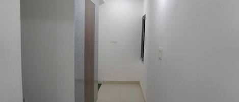 A narrow, well-lit hallway with white walls and a tiled floor, leading to a staircase.