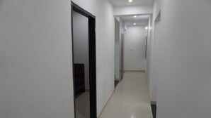 A narrow, well-lit hallway with white walls and a black-framed door on the left. - Hotel Shree Radhe Laxmi (Khatoo)