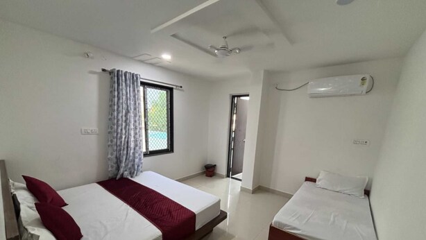 A hotel room with two single beds, a ceiling fan, an air conditioning unit, and a window with curtains. - Hotel Shree Radhe Laxmi (Khatoo)