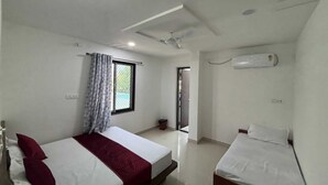 A small, compact hotel room with a single bed, a small table, a window with a view, and a ceiling fan. - Hotel Shree Radhe Laxmi (Khatoo)