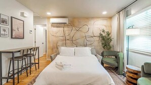 Una habitación de hotel moderna con una cama grande, un escritorio con sillas, un sillón verde y una planta.