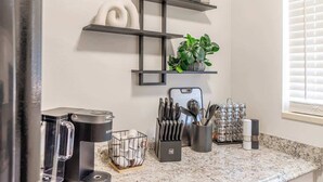 Una cocina con cafetera, bloque de cuchillos y una planta en un estante.