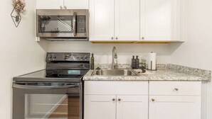 Una cocina con armarios blancos, un microondas de acero inoxidable, una estufa y un lavabo.