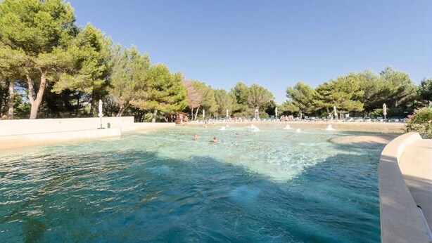 A clear pool surrounded by trees and a sandy beach area. - Apartment in Provence With Heated Pool (Mallemort)