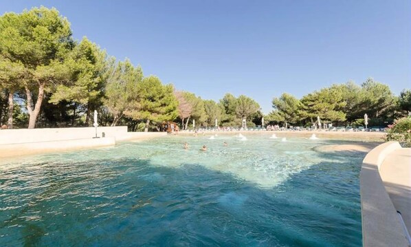 A clear pool surrounded by trees and a sandy beach area. - Apartment in Provence With Heated Pool (Mallemort)
