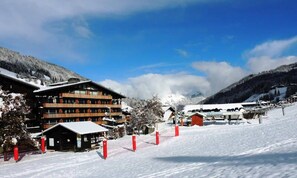 Een met sneeuw bedekte wintersportplaats met een berghut met meerdere verdiepingen en een berg op de achtergrond.