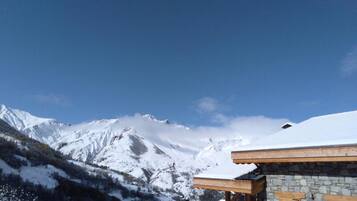 A mountain lodge with a stone facade and wooden beams, set against a backdrop of snow-covered peaks and a clear blue sky.