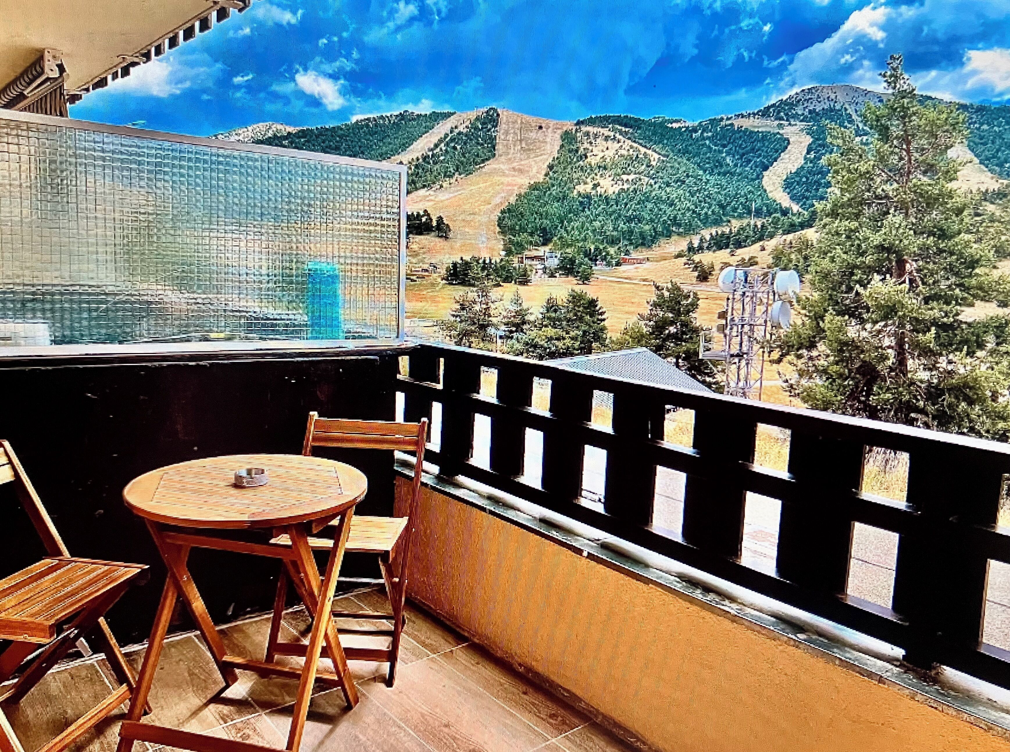 A balcony with a table and chairs, overlooking a mountainous landscape with trees and power lines.