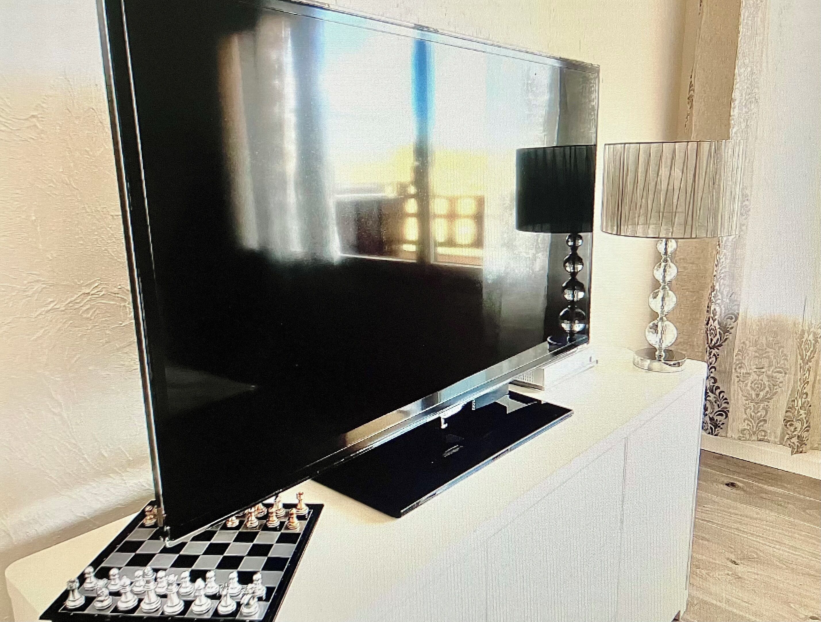 A flat-screen TV on a stand with a chessboard in front.