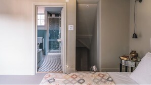 Et soveværelse med en seng, et natbord med lampe, samt udsigt til et badeværelse med bruser og toilet.