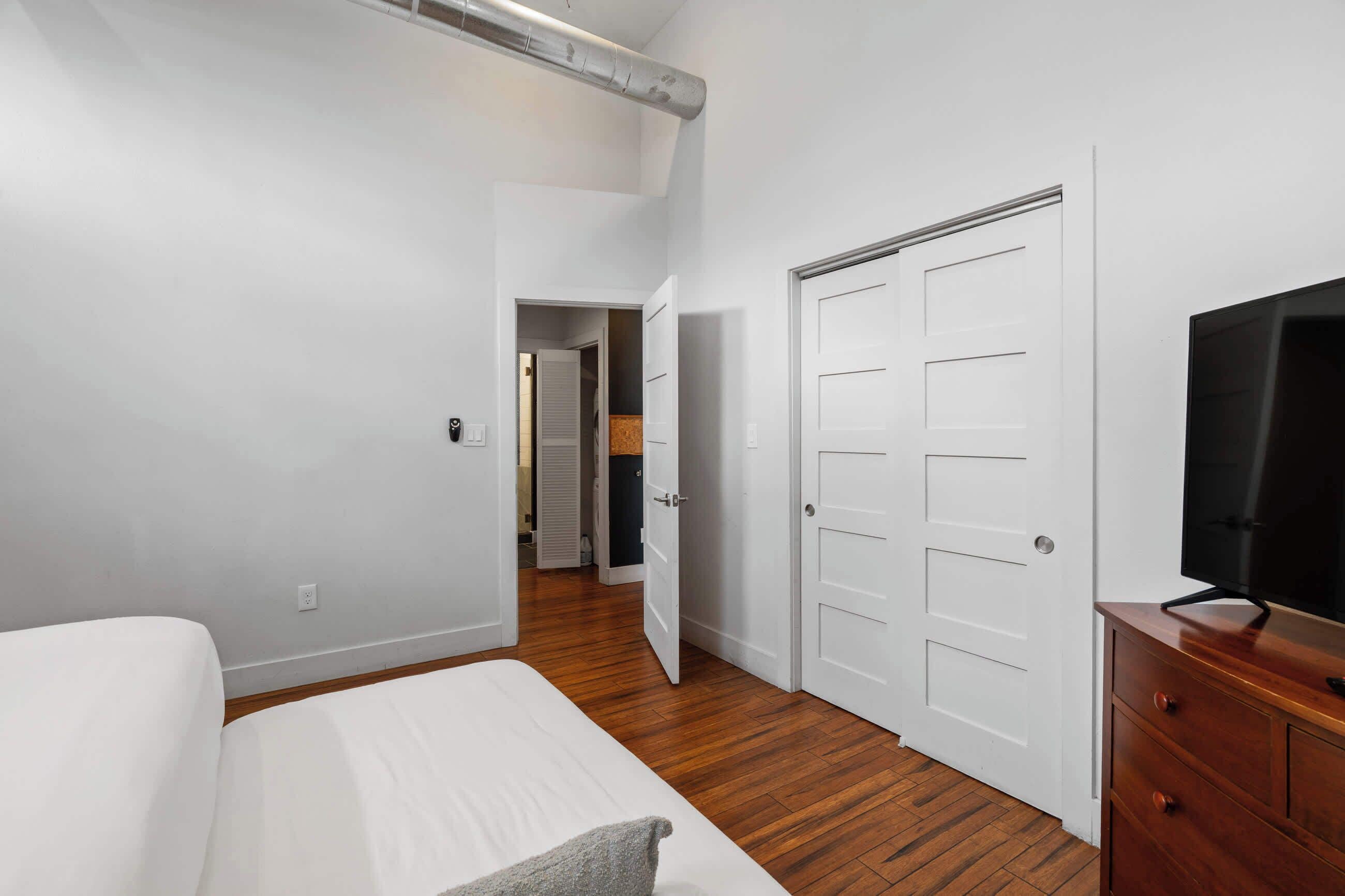 A bedroom with a bed, a dresser, a TV, and a closet.