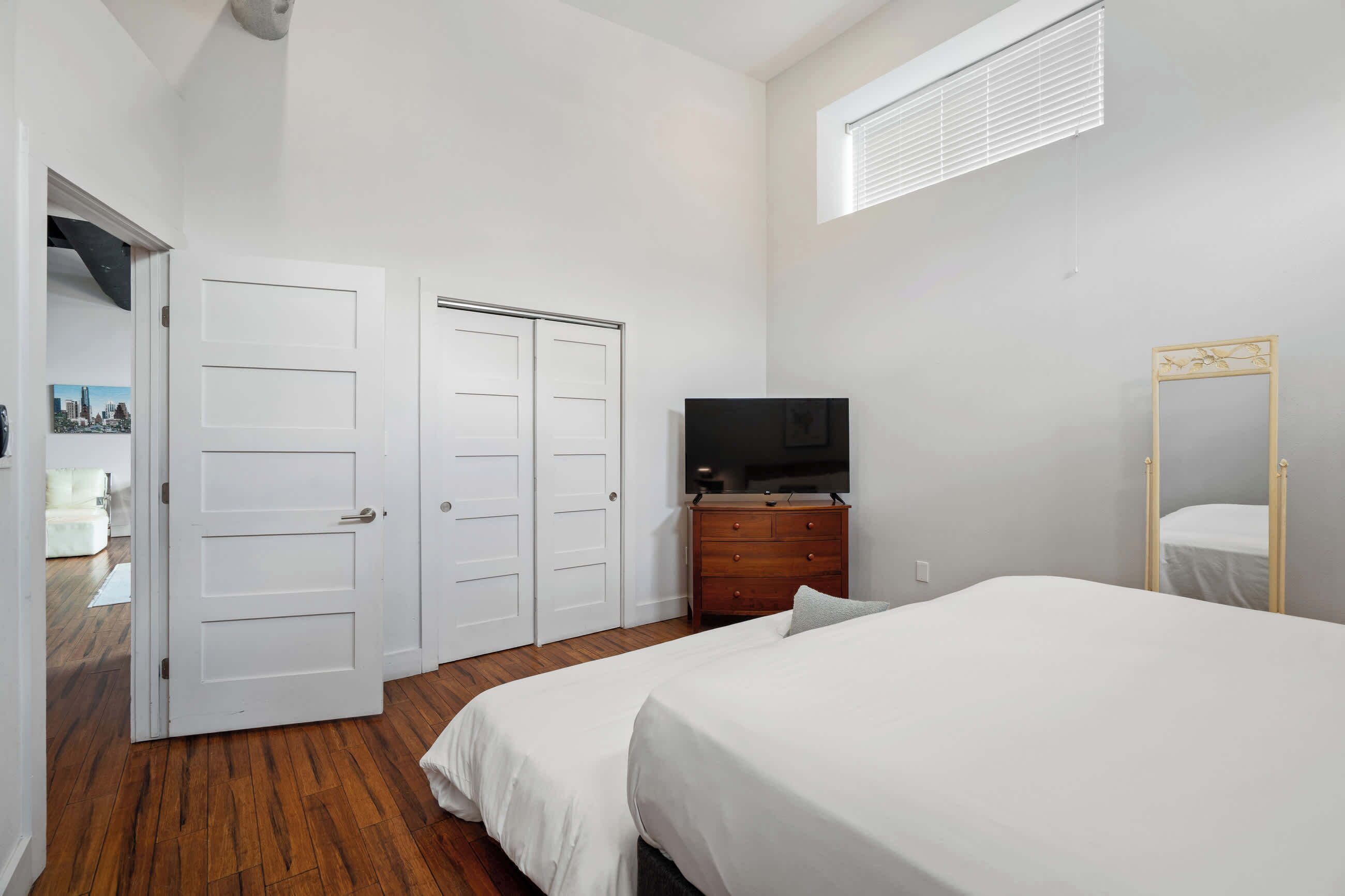 Quarto com cama, cômoda, televisão e espelho.