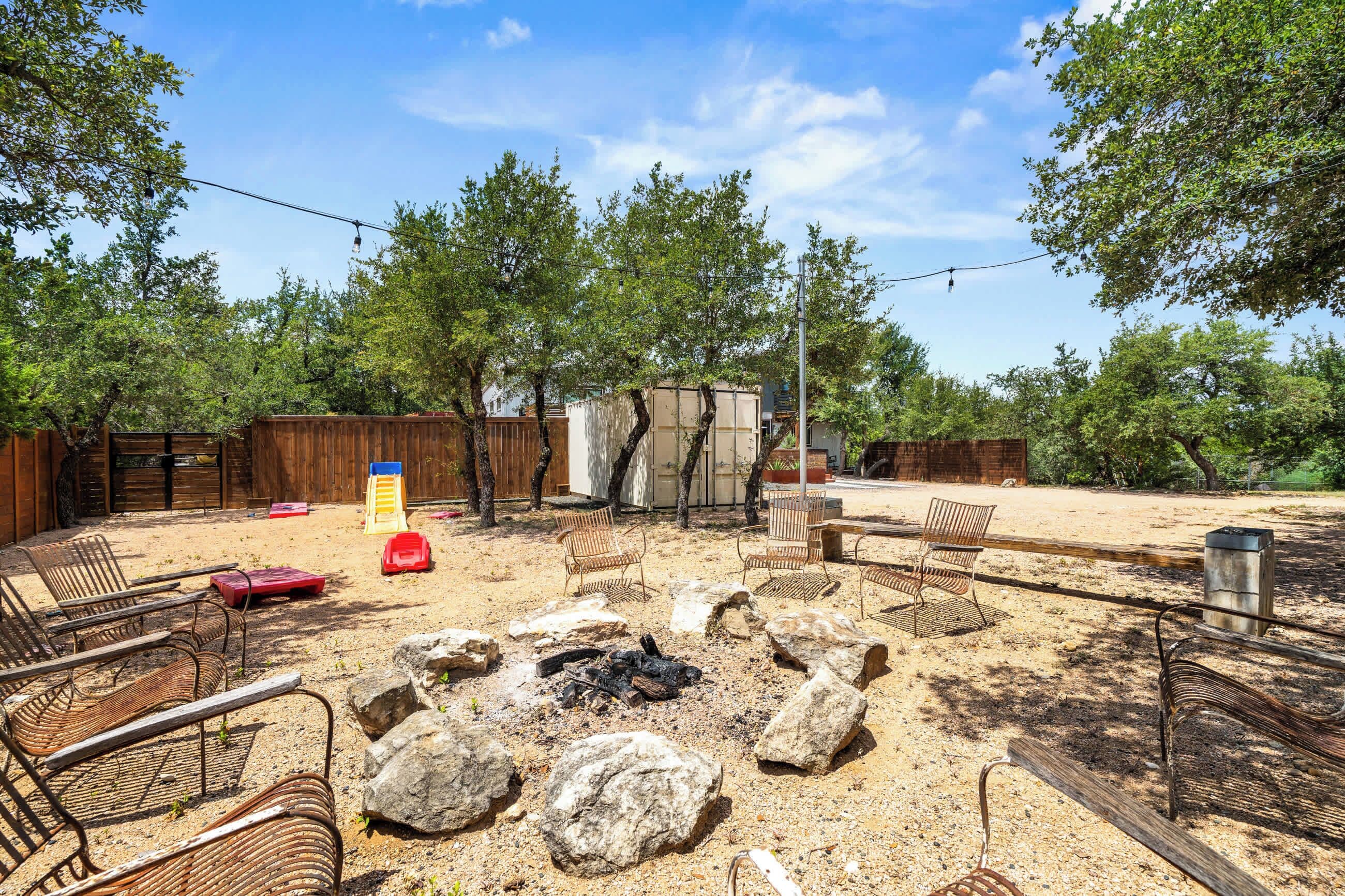 An outdoor patio area with a fire pit, seating, and a wooden fence.