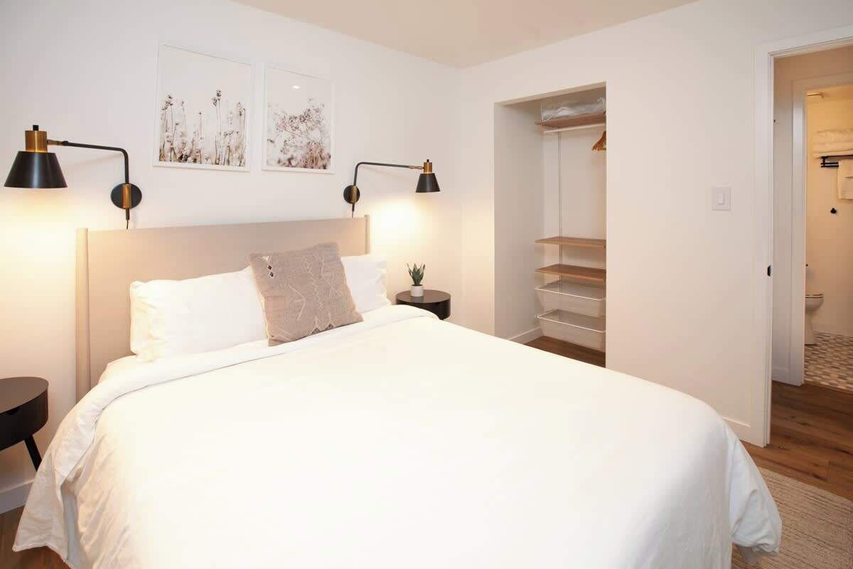 Un dormitorio con una cama grande, dos lámparas de noche, una mesita de noche y una estantería de pared.
