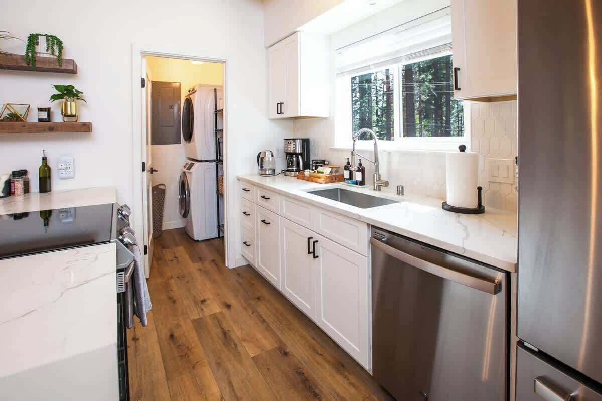 A modern kitchen with white cabinets, a stainless steel refrigerator, a dishwasher, and wooden flooring.