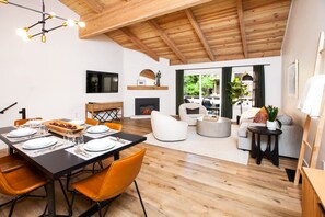 A spacious living area with a fireplace, a dining area with orange chairs, and a view of the outdoors through large windows.