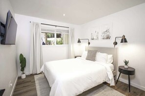 Ein modernes Schlafzimmer mit einem großen Bett, einem an der Wand montierten Fernseher und einem Fenster mit Vorhängen.