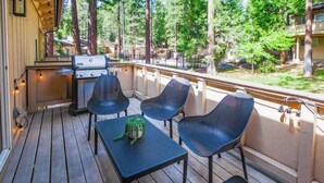 Eine Holzterrasse mit Sitzgelegenheiten im Freien, einem Grill und Blick auf ein bewaldetes Gebiet.