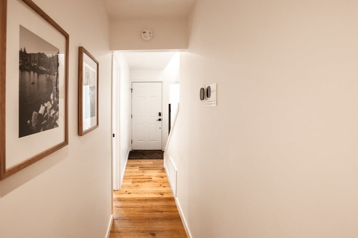A hallway with wooden flooring, white walls, and framed pictures on the left.