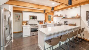 A modern kitchen with wooden beams, stainless steel appliances, and a central island with bar stools. - The Canoe Cabin in Incline Village (Incline Village)