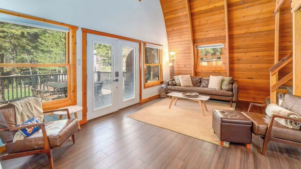 A spacious living room with a high ceiling, wooden walls, and large windows offering a view of the outdoors. - The Canoe Cabin in Incline Village (Incline Village)
