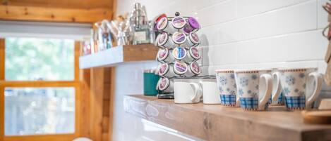 A kitchen with wooden cabinets, a coffee machine, and a variety of mugs on a shelf.