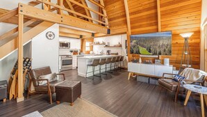 A spacious living area with a high ceiling, wooden beams, a kitchen with a central island, and a large painting of a forest. - The Canoe Cabin in Incline Village (Incline Village)