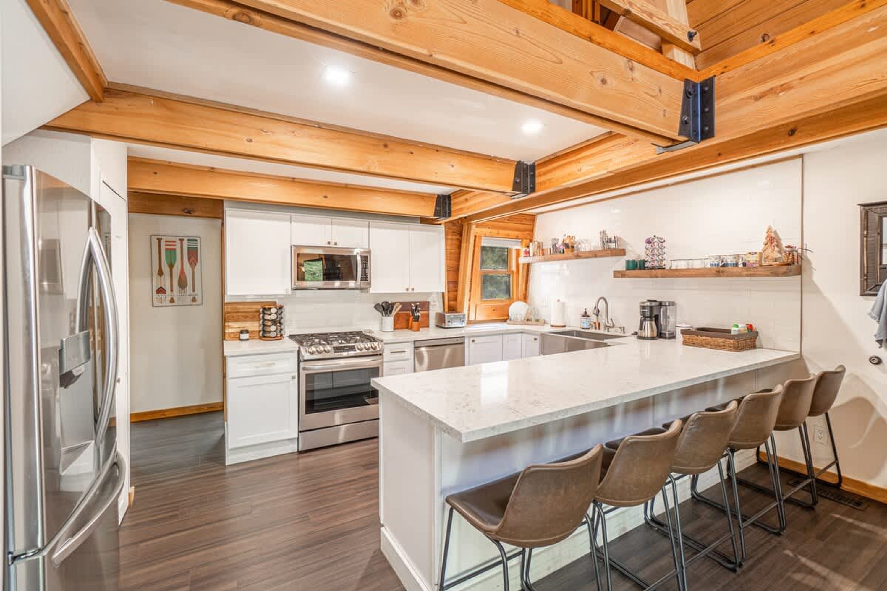 A modern kitchen with a central island, stainless steel appliances, and wooden ceiling beams.