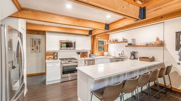 A modern kitchen with a central island, stainless steel appliances, and wooden ceiling beams.