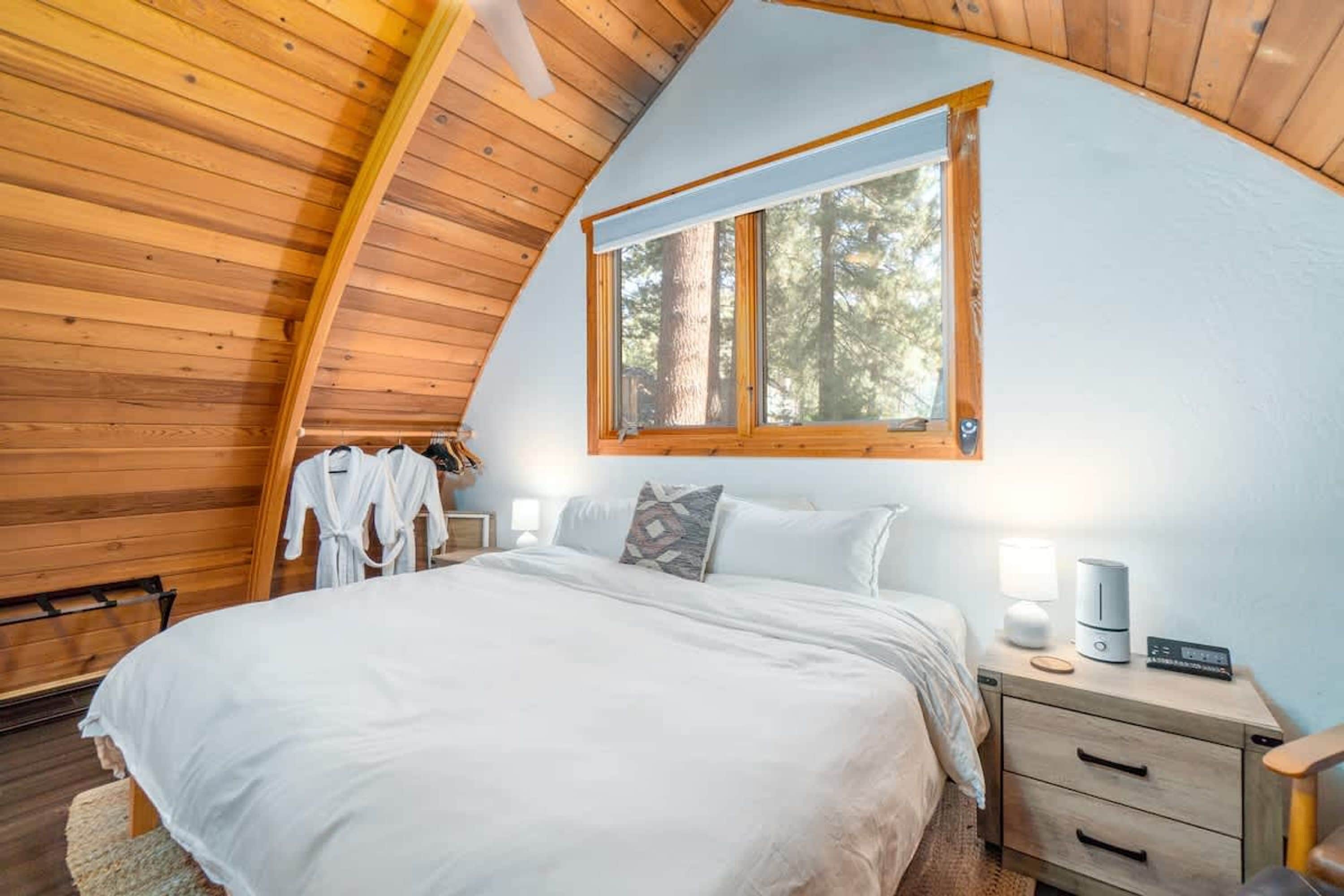 A bedroom with a bed, bedside tables, a window, and a wooden ceiling.