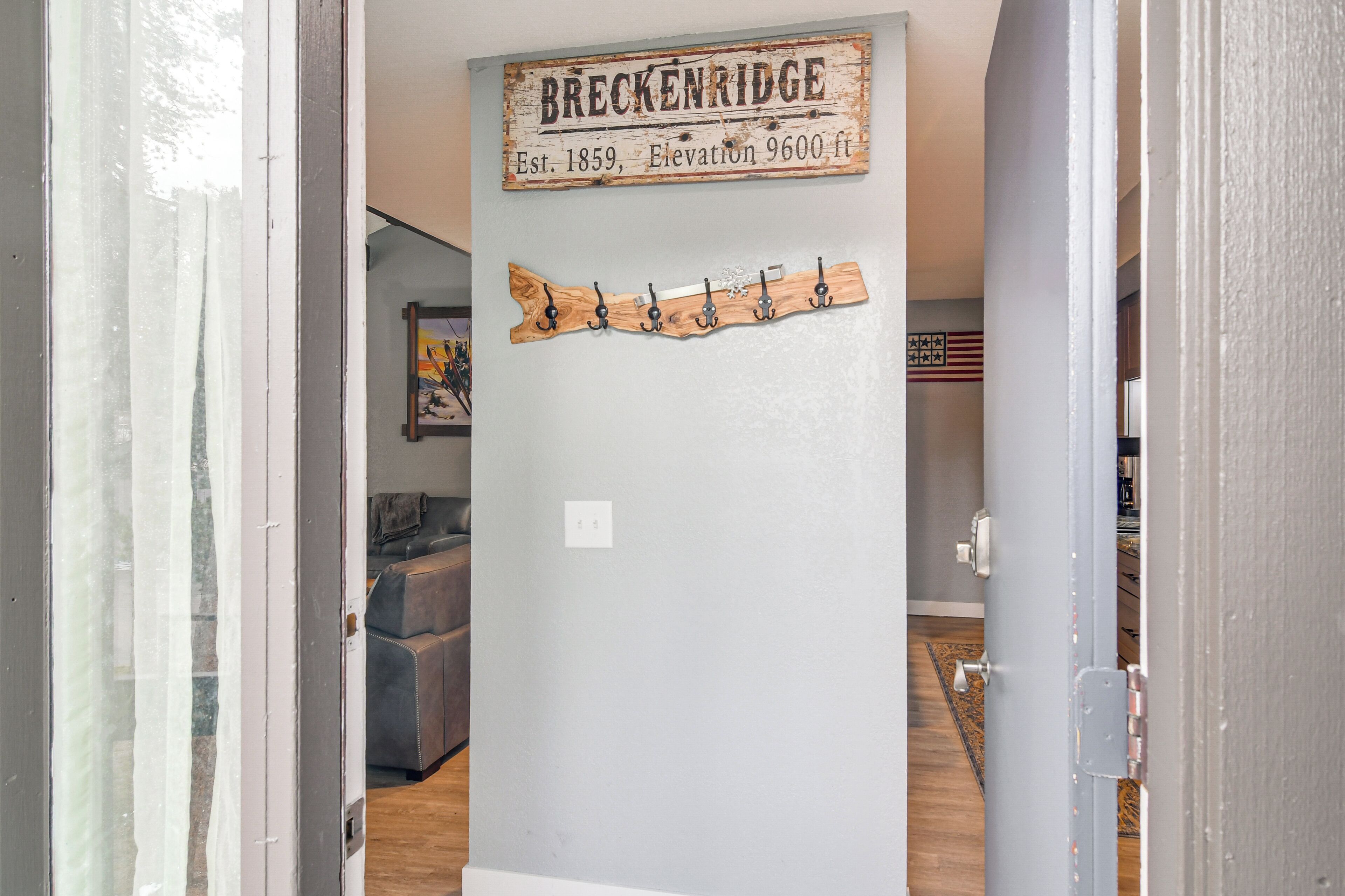 A hallway with a wooden sign reading "BRECKENRIDGE, Est. 1859, Elevation 9600 ft." and a wooden wall-mounted rack with hooks.